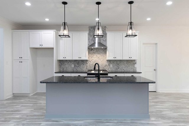 Kitchen remodel featuring large island with black countertop and gray herringbone tile backsplash