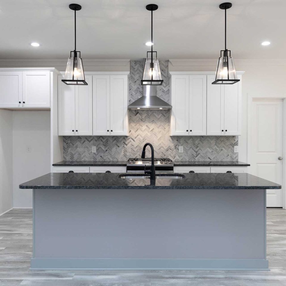 Kitchen remodel featuring large island with black countertop and gray herringbone tile backsplash