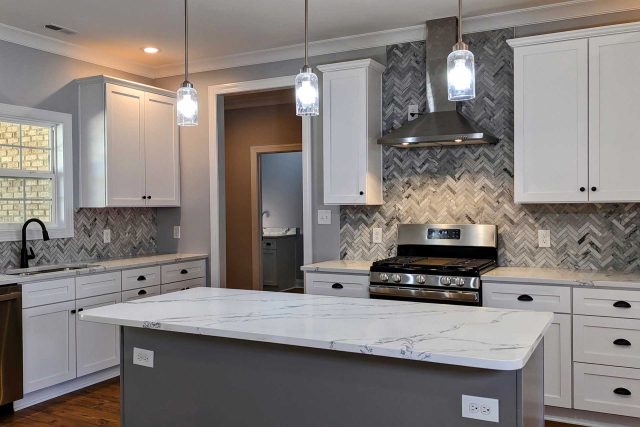 Kitchen remodel featuring large island with white countertop and gray herringbone tile backsplash