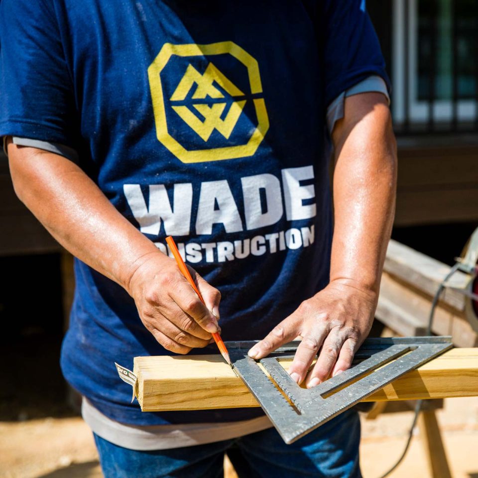 A professional handyman working for Wade Construction in Rock Hill, SC uses a triangular ruler to mark measurements on a piece of lumber