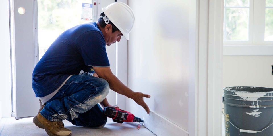 A professional handyman installs a white baseboard during a home remodel by Wade Construction in Rock Hill, SC