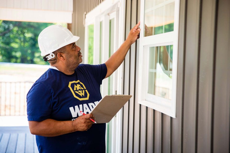 A general contractor in a white hard hat reviews the exterior of a window frame