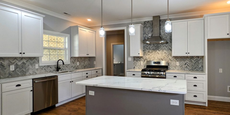 Newly remodeled kitchen featuring wood flooring, a center island, herringbone tile backsplash, and white cabinetry by Wade Construction in Rock Hill, SC