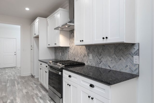 Kitchen in a new home construction featuring herringbone tile backsplash, black countertops and white cabinetry by Wade Construction in Rock Hill, SC