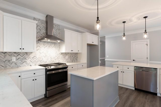 Kitchen remodel featuring large island and hanging lights with white countertops and gray backsplash