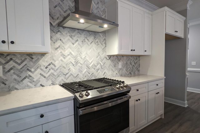 Kitchen remodel featuring gas stove with white countertops and gray stone backsplash