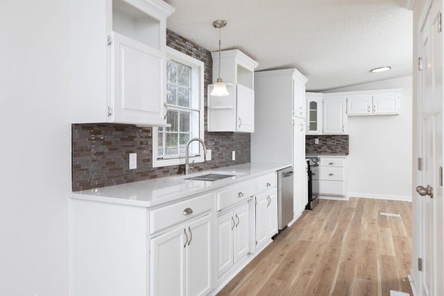 Newly remodeled kitchen featuring brown stone backsplash, white cabinetry, and light wood flooring,