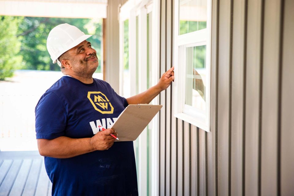 A general contractor in a white hard hat reviews the exterior of a window frame