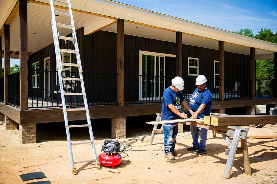 two men in blue shirts working on upgrading the exterior of a home